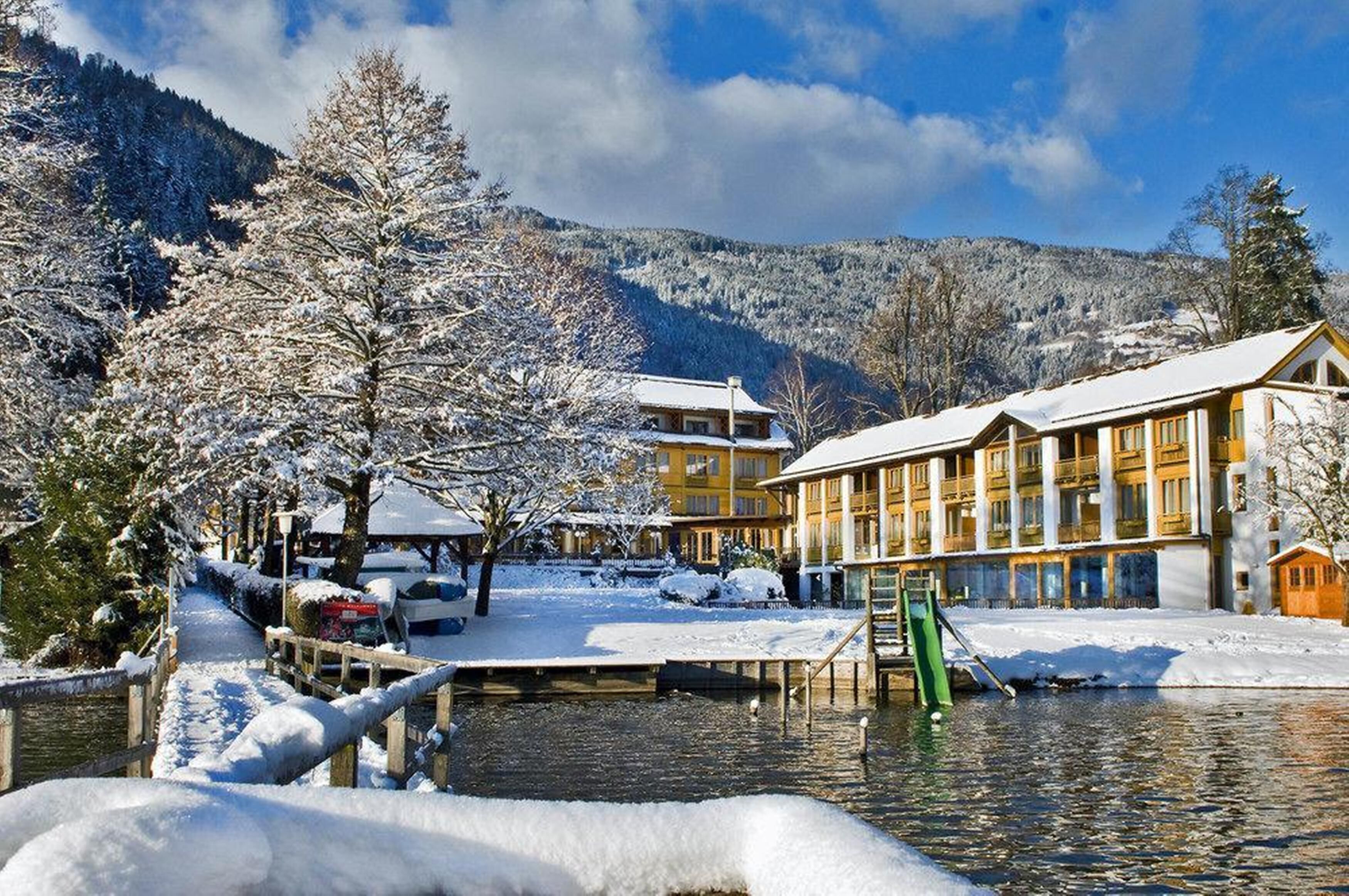A hotel with a snow-covered exterior, a dock extending into a lake, and mountains in the background.