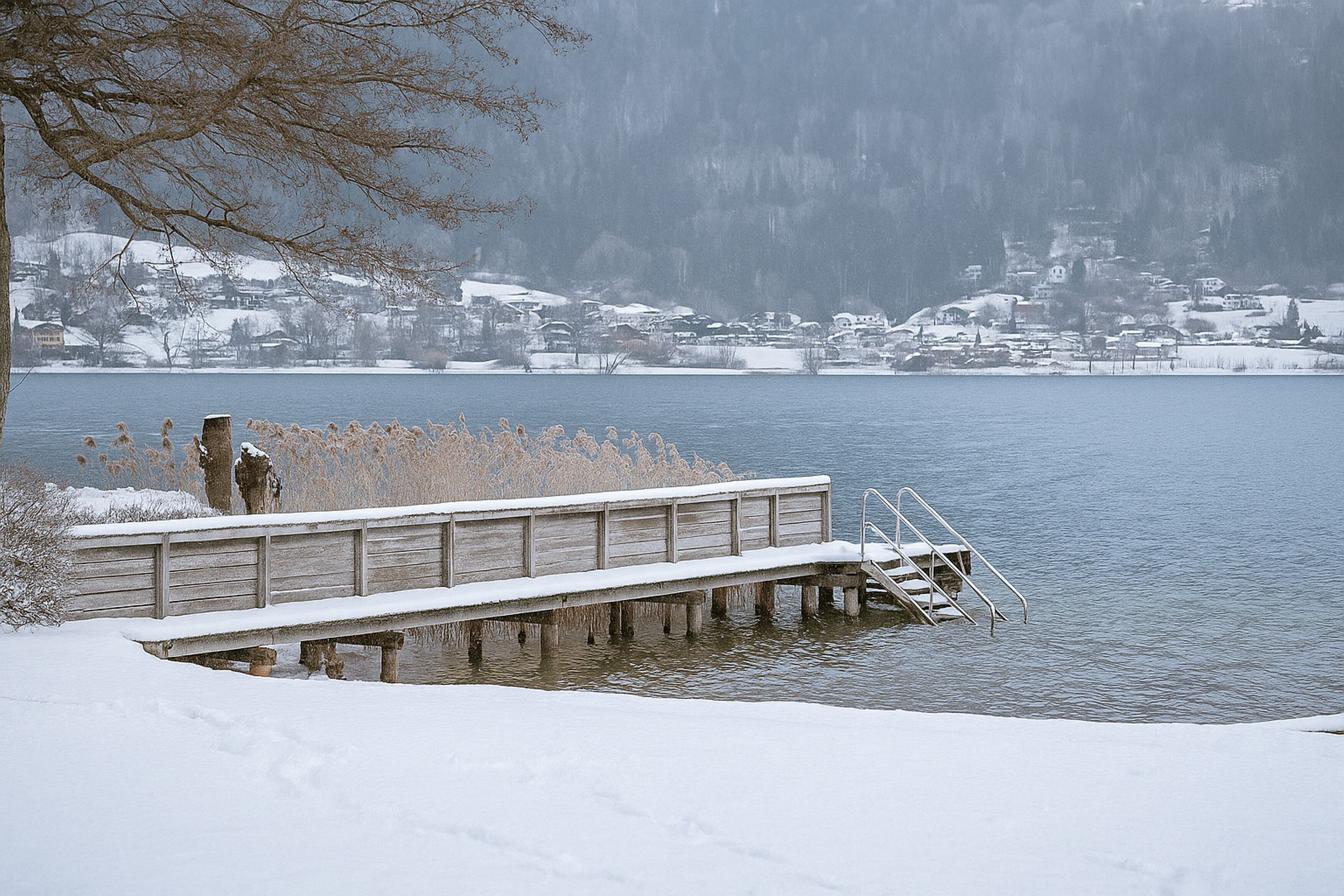 Un muelle cubierto de nieve que se adentra en un lago, con un pueblo al fondo.