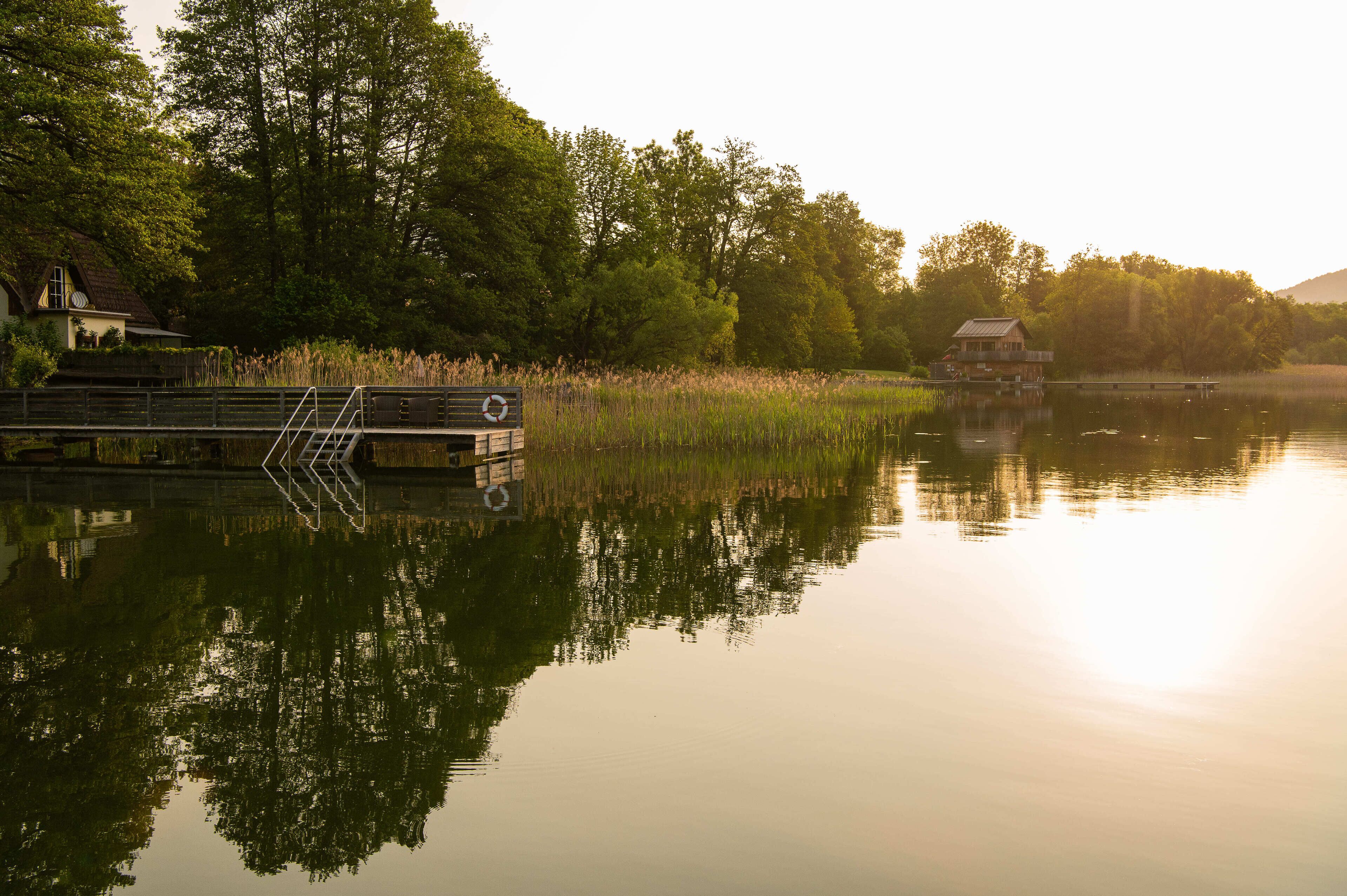 Un lago tranquilo con un muelle de madera y una casa a la izquierda.