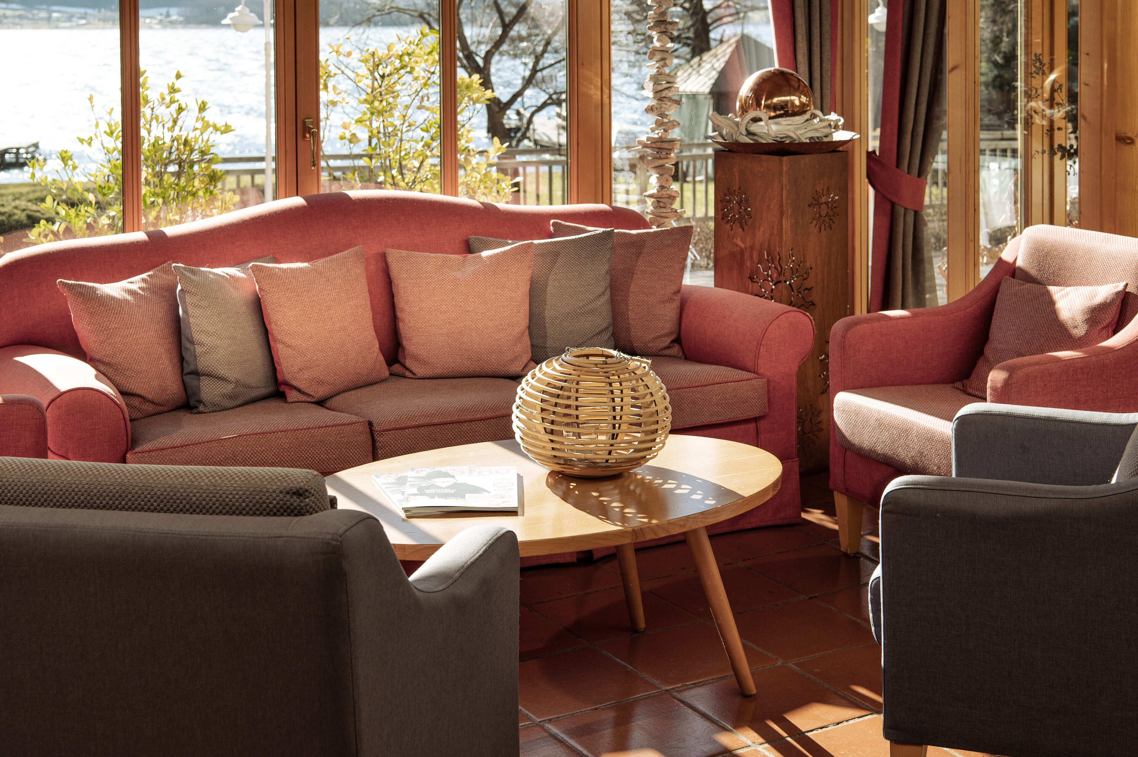 A cozy living room with a red sofa, a wooden coffee table, and a view of a body of water through large windows.