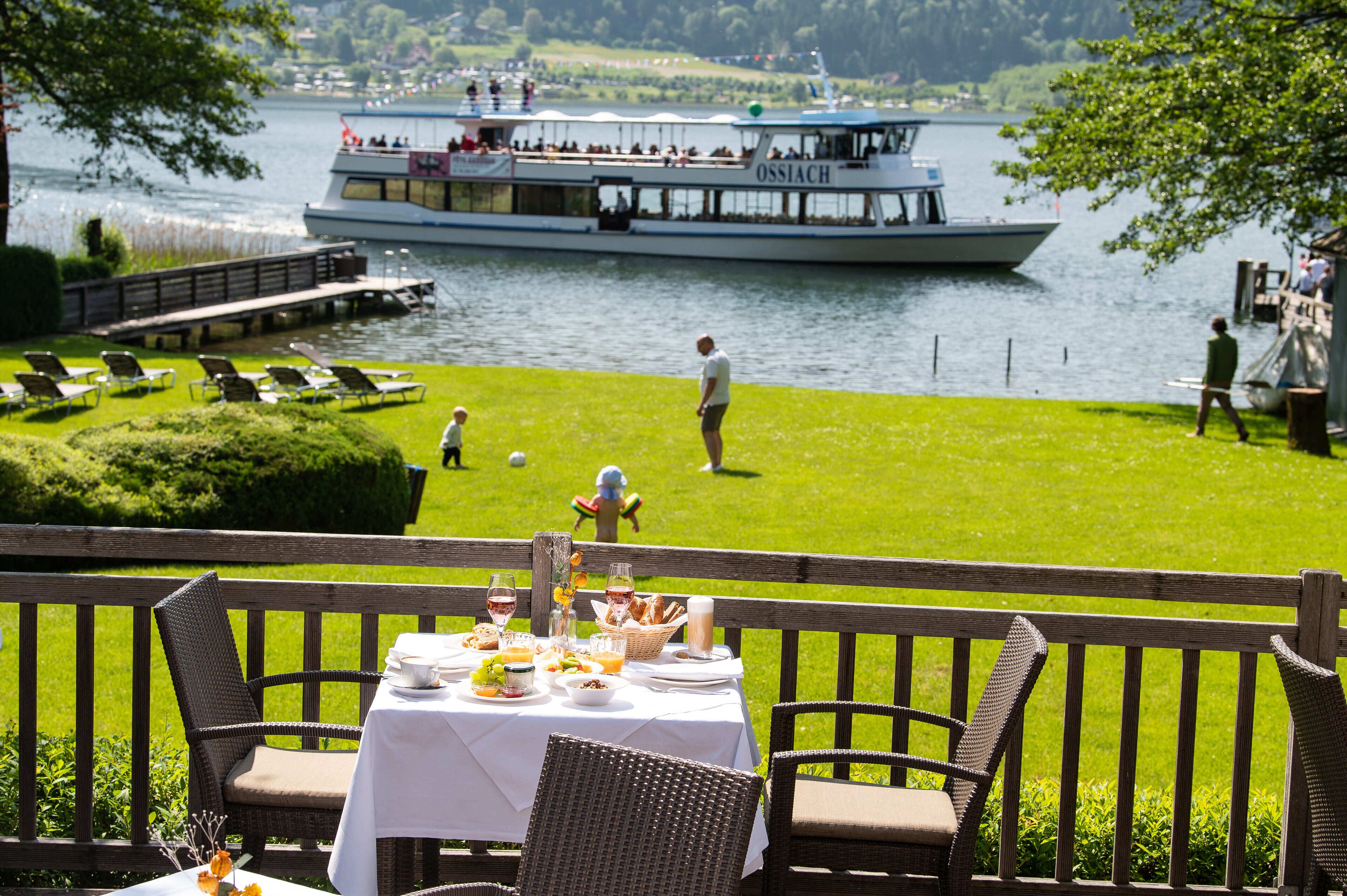 Zona de comedor junto al lago con una mesa preparada para una comida, con vista a un lago y un bote.