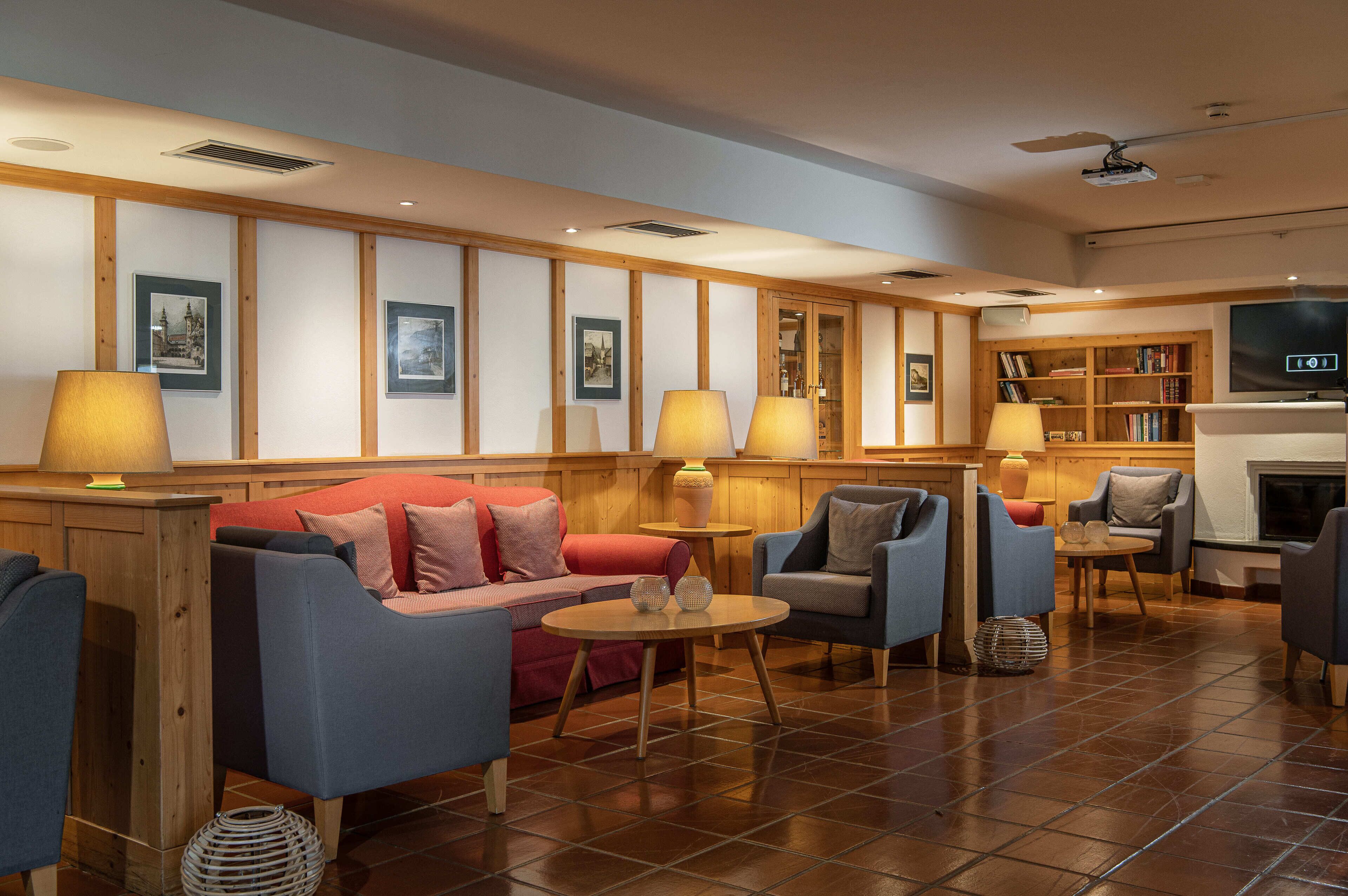 A hotel lobby with a red sofa, blue armchairs, a fireplace, a bookshelf, and a television.