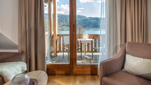 Une pièce dotée d’un plancher en bois, de deux canapés, d’une table et offrant une vue sur un lac et des montagnes, visible à travers une porte vitrée.