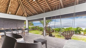 Un espace extérieur abrité, doté d’une terrasse en bois, de meubles en osier et offrant une vue sur l’océan.