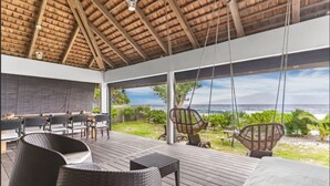 Un espacio al aire libre techado con terraza de madera, mobiliario de mimbre y vista al océano.