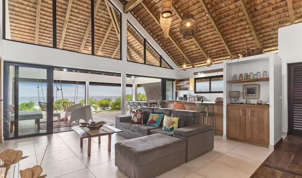 Een ruime woonkamer met een groot raam met uitzicht op de oceaan, een keuken met houten kasten en een eethoek met panoramisch uitzicht.