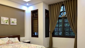 A bedroom with a bed, a window with curtains, a wall-mounted shelf, and two framed pictures. - 3-bedroom townhome in enchanting Đà Nẵng with WiFi, AC, fitness room (Đà Nẵng)