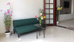 A green sofa, a small round table with a vase of flowers, and a potted plant with pink flowers. - 3-bedroom townhome in enchanting Đà Nẵng with WiFi, AC, fitness room (Đà Nẵng)