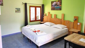Une chambre avec un lit, une tête de lit en bois, une fenêtre avec des rideaux, un tableau au mur et une table avec une chaise.