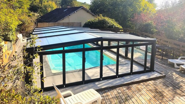 Une piscine dotée d’une enceinte en verre, entourée d’une terrasse en bois et avec une maison en arrière-plan.