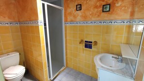 Une salle de bain avec des carreaux jaunes, des toilettes blanches, une douche et un lavabo avec un miroir.
