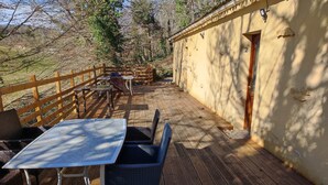 Une terrasse en bois, agrémentée de mobilier d’extérieur, notamment une table et des chaises, jouxtant un bâtiment doté d’une porte et de fenêtres.