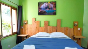 Une chambre avec un lit, deux tables de chevet, une fenêtre et un tableau représentant une cascade accroché au mur.