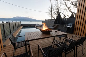 Een houten terras met een pooltafel, stoelen en een vuurkorf.