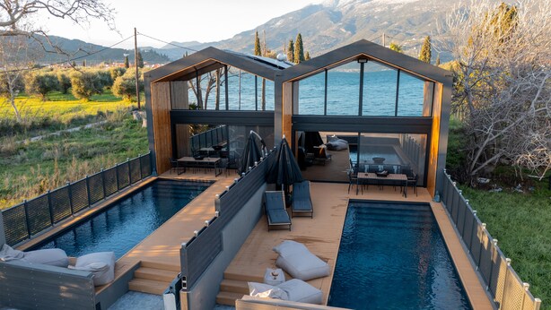 Un área de piscina moderna al aire libre con dos piscinas separadas, mobiliario de terraza de madera y vistas al lago.
