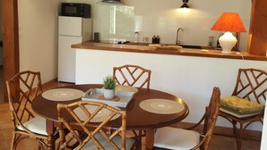 Una cucina compatta con forno a microonde, piano cottura e lavello. C'è un tavolo da pranzo con sedie e una piccola pianta in vaso.