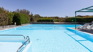 A swimming pool with multiple lanes, surrounded by greenery and a covered seating area.