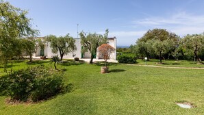 A well-maintained garden with a variety of trees and shrubs, a pathway, and a building with a white facade and green accents.