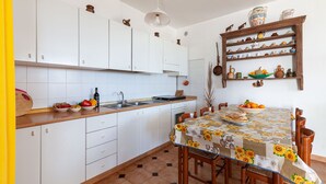 A kitchen with white cabinets, a wooden countertop, a dining table with a sunflower tablecloth, and a shelf with kitchenware.