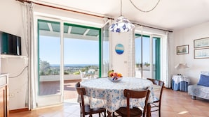 A dining area with a table set for four, a television on the left, and a balcony with a view. - Villa Giorgisa Apartment 2 Pool Sea View (Ugento)