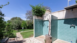 An outdoor shower area with stone flooring, a wooden deck, and a green-tiled wall. - Villa Giorgisa Apartment 2 Pool Sea View (Ugento)