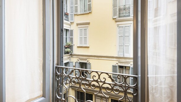 Vista desde un balcón con barandilla de hierro forjado, que da a un edificio con varias ventanas y balcones.