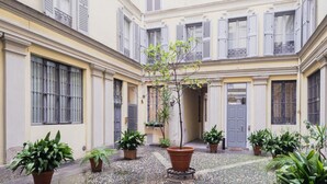 Un patio con plantas en macetas, un árbol central y un edificio con múltiples ventanas y balcones.