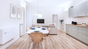 Una cocina moderna con armarios blancos, una mesa de comedor con sillas y un televisor de pantalla plana montado en la pared.