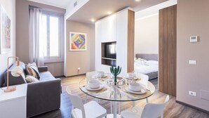 Una habitación de hotel moderna con zona de comedor, sofá, televisión y cama.