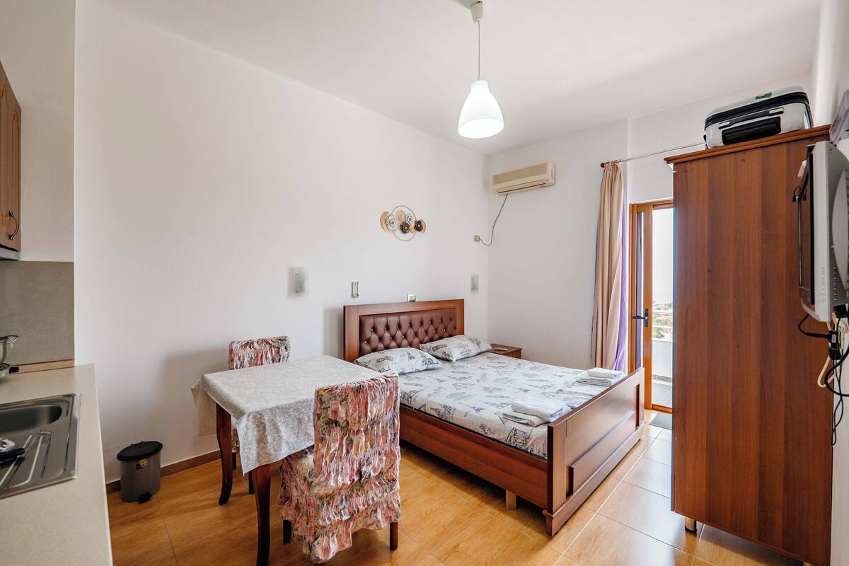 Un dormitorio compacto con cama, una mesita, una silla, armario y kitchenette.