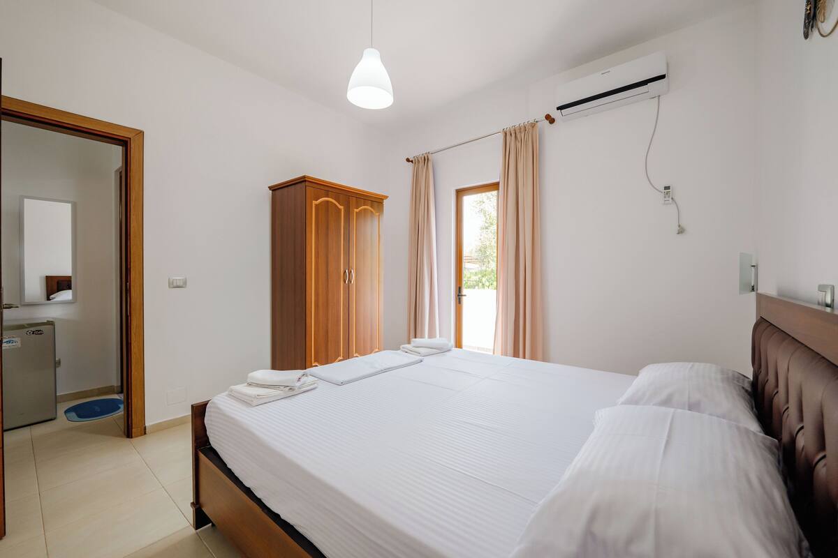 Un dormitorio con una cama grande, un armario de madera y un baño a la vista a través de una puerta abierta.
