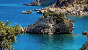 Un paisaje costero con aguas azules cristalinas, afloramientos rocosos y una ciudad al fondo.