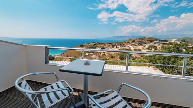 Un balcón con dos sillas y una mesa, con vistas a un pueblo costero y al mar.