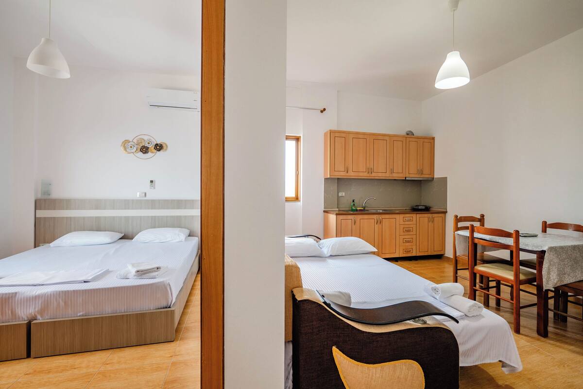 Un dormitorio con una cama, mesitas de noche y una ventana. El suelo es de madera y la pared es blanca.