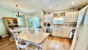 A kitchen with a central island, white cabinetry, a dining area with chairs, and a chandelier. - Suncatcher on the Loop - 2/2 w/ Golf Cart in The Village of Lynnhaven (The Villages)