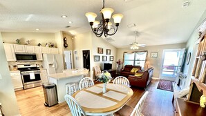 A spacious kitchen with modern appliances, a dining area with a round table and chairs, and a cozy living room with a sofa and a TV. - Suncatcher on the Loop - 2/2 w/ Golf Cart in The Village of Lynnhaven (The Villages)