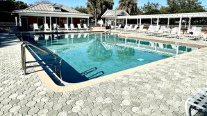 A swimming pool with hexagonal tiles, lounge chairs, and covered areas with umbrellas. - Suncatcher on the Loop - 2/2 w/ Golf Cart in The Village of Lynnhaven (The Villages)
