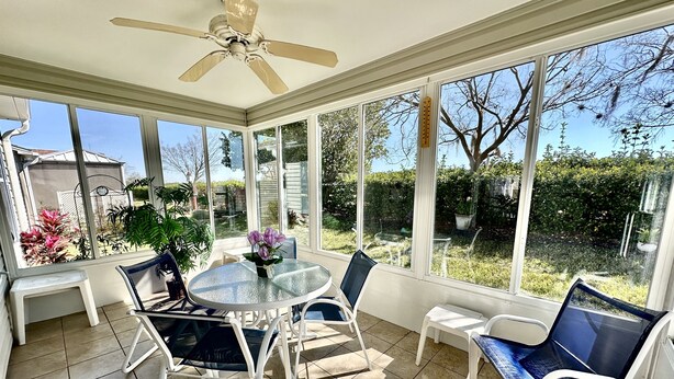 A sunroom with a glass table and chairs, a ceiling fan, and a view of the garden. - Suncatcher on the Loop - 2/2 w/ Golf Cart in The Village of Lynnhaven (The Villages)