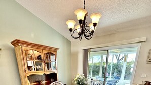 A dining area with a round table, white chairs, a wooden cabinet with glass doors, and a chandelier. - Suncatcher on the Loop - 2/2 w/ Golf Cart in The Village of Lynnhaven (The Villages)