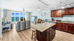 A modern kitchen with wooden cabinets, a central island, and a dining area with a view of the ocean. - Luxurious 4BD! Oceanview! Free Beach Chair Service! (Panama City Beach)