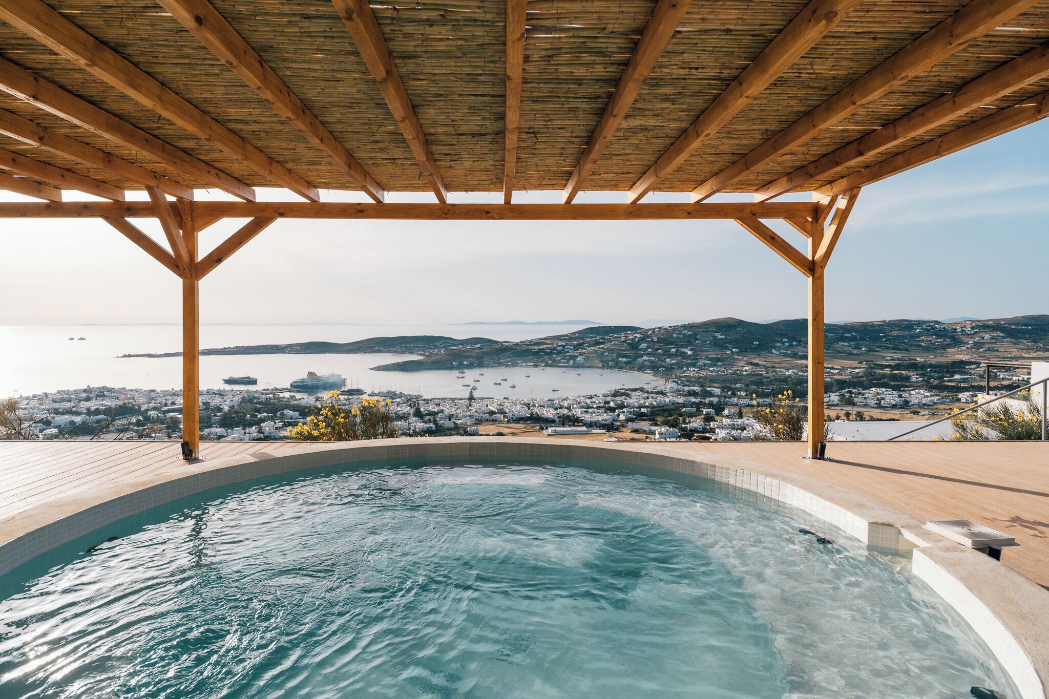 Un bain à remous surmonté d’une pergola en bois, offrant une vue sur une ville côtière et la mer.