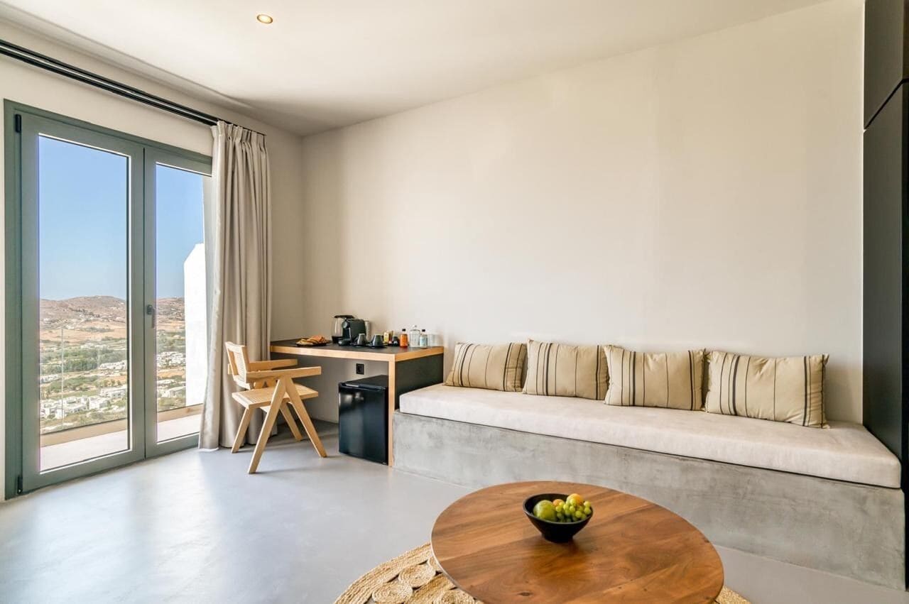A modern room with a large window, a sofa, a dining table, and a kitchen area.