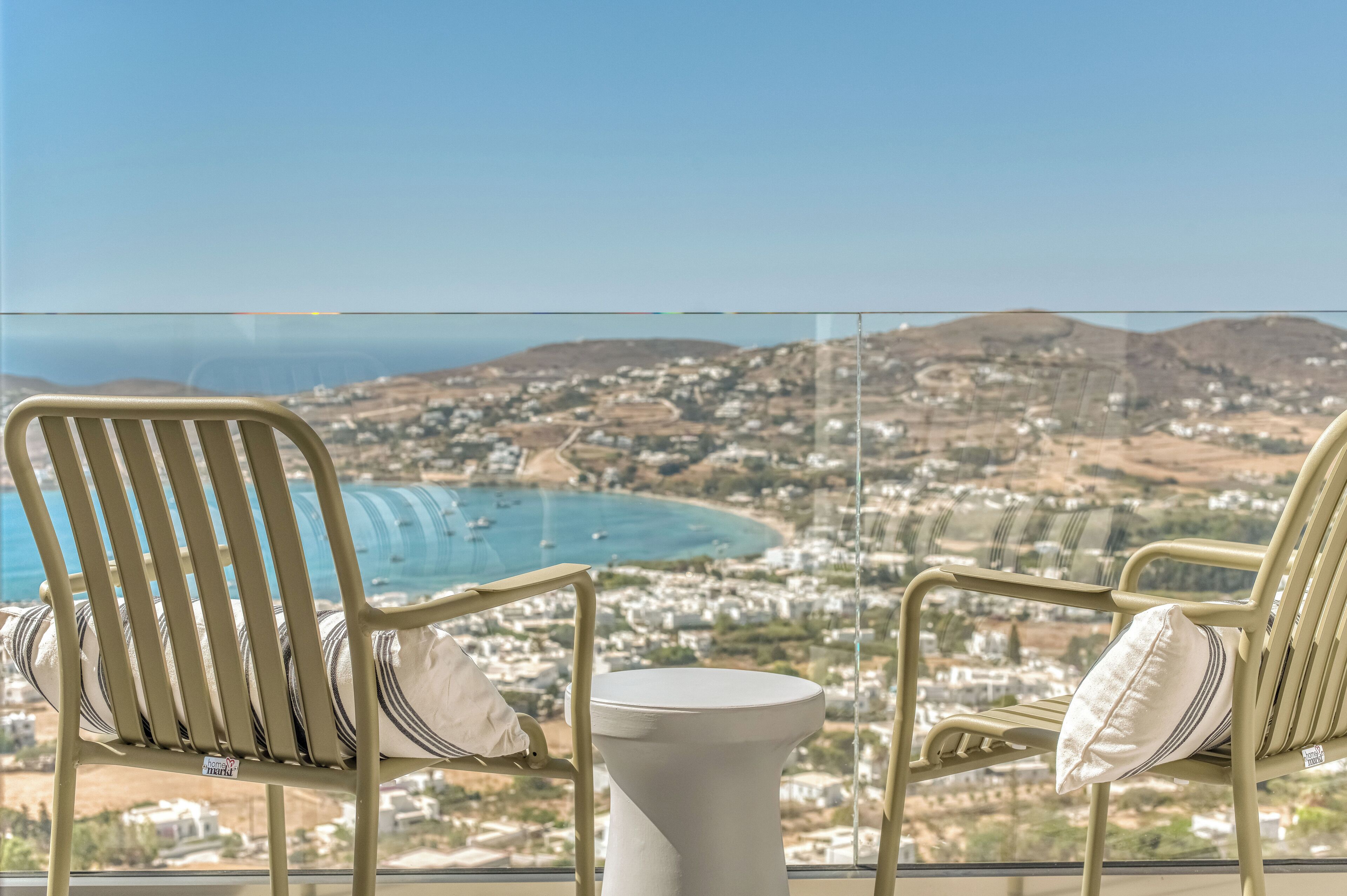 Two beige chairs with striped cushions and a small white table in front, overlooking a coastal town and the sea.