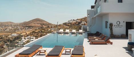A rooftop pool area with lounge chairs and a view of a hillside town.