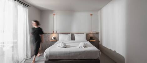 A modern hotel room with a large bed, bedside tables, and a view of the city through sheer curtains.