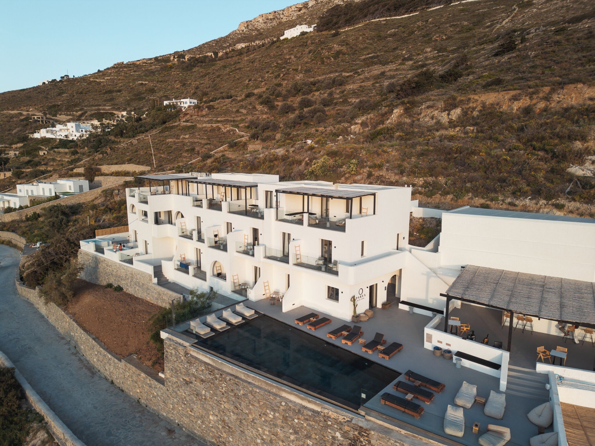 A modern multi-story building with a rooftop pool area, surrounded by a hilly landscape.