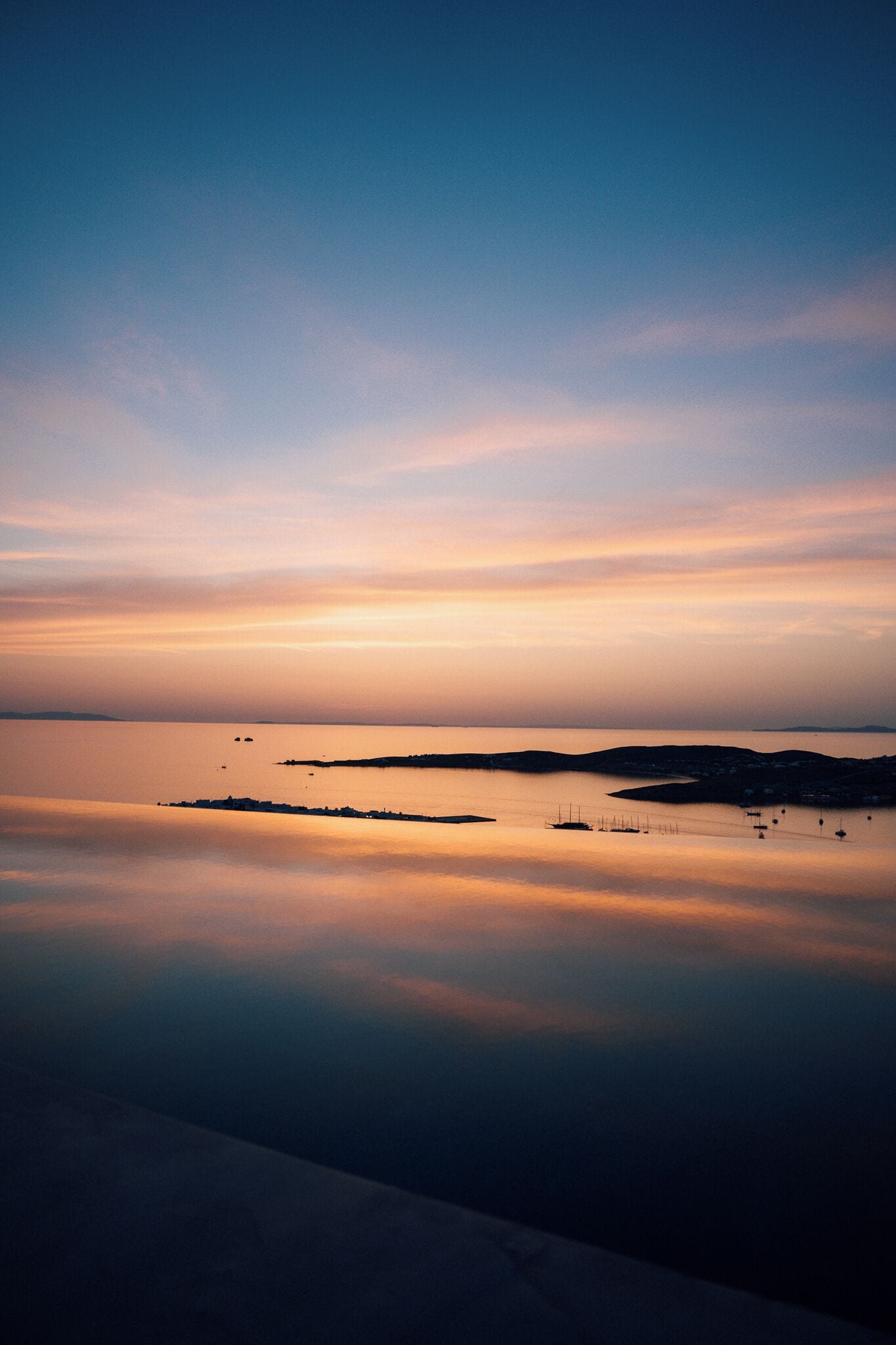 A calm sea at sunset with distant land and a clear sky.