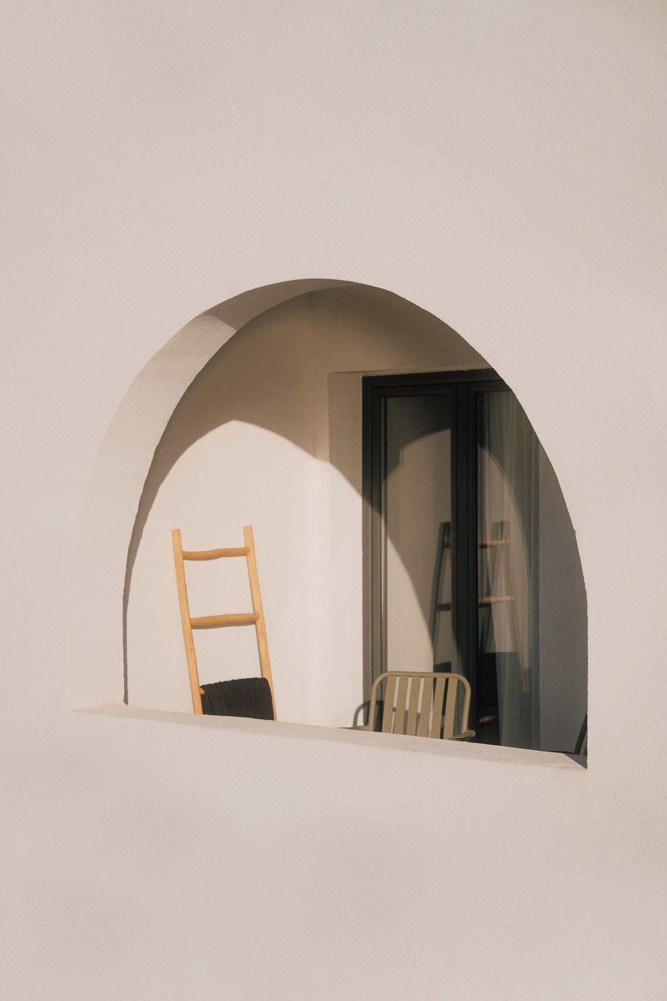 Una habitación con una pared blanca, una escalera de madera apoyada en ella y una silla.