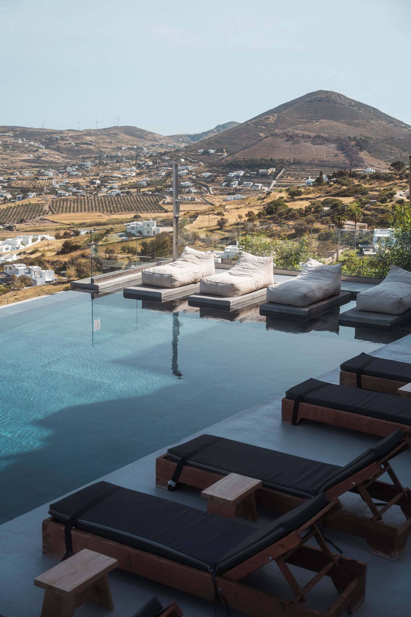 Una piscina infinita con sillas de descanso y vistas a un pueblo en la ladera.