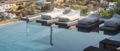 Una piscina infinita con sillas de descanso y vistas a un pueblo en la ladera.